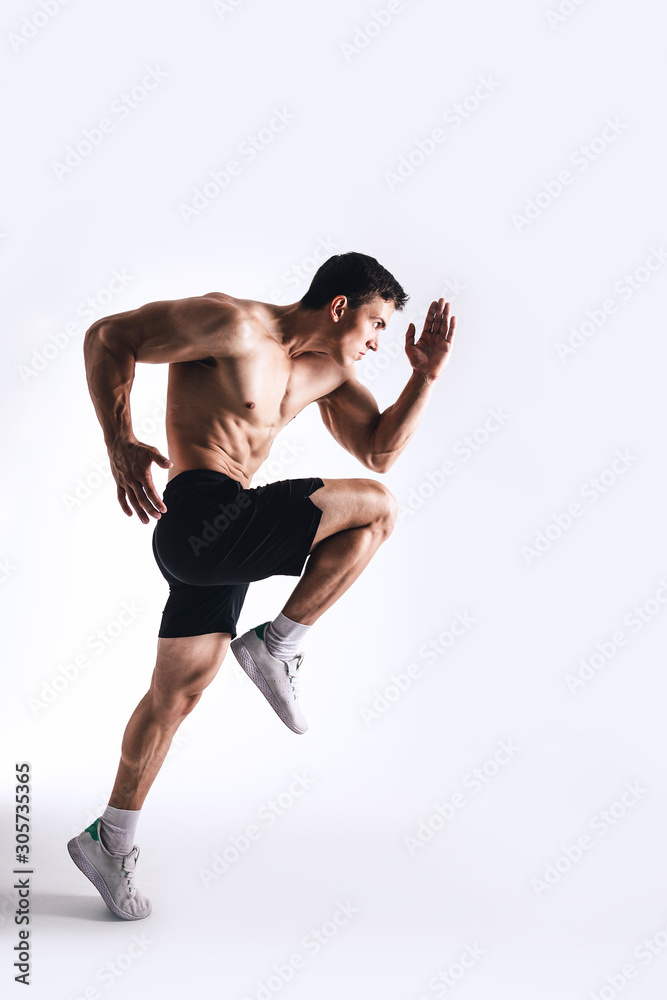 Muscle male model in black sports shorts and white sneakers in a jumping pose on white background. Sports motion concept. Studio shot.