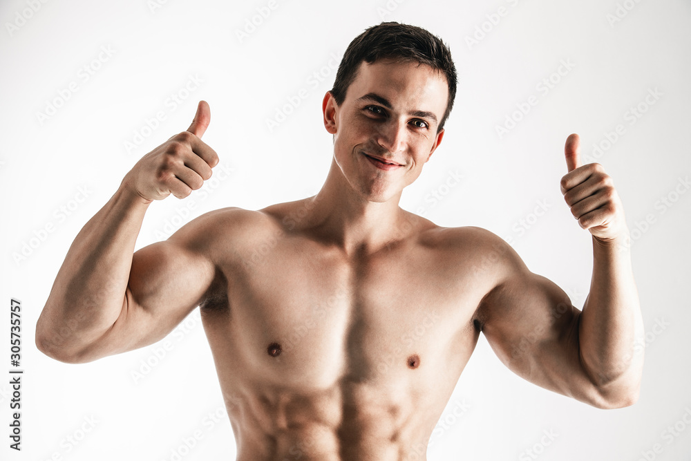 Fototapeta premium Portrait of handsome young man showing thumbs up over white background. Perfect hair & skin. Close up. Studio shot