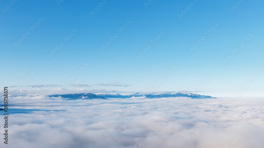 Valley in the mountains covered with snow above the clouds blue sky.