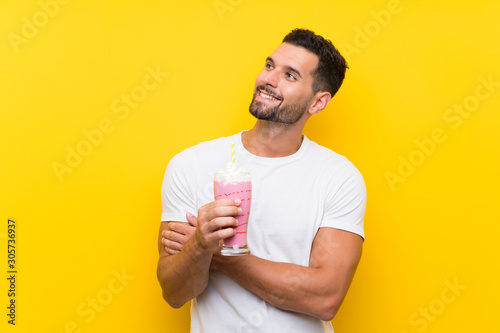 Young man with strawberry milkshake over isolated yellow background looking up while smiling © luismolinero