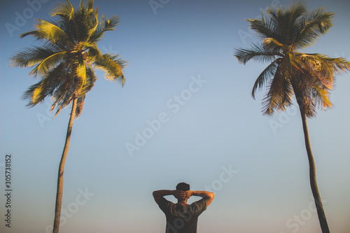 Joven tranquilo viendo a la playa con palmeras