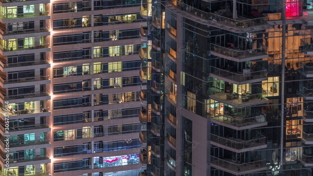 Rows of glowing windows with people in apartment building at night.