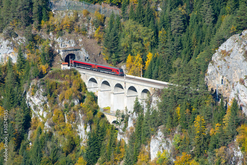 Red train on a viaduct between two tunnels on the Semmering Railway. The Semmering Railway is the oldest mountain railway of Europe and a Unesco World Heritage site.