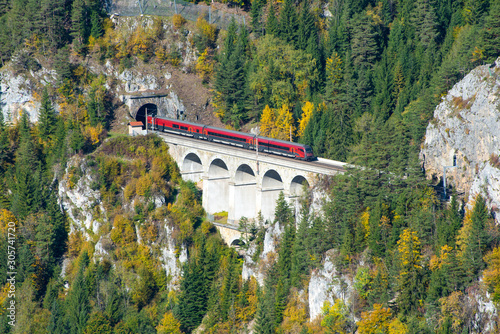 Red train on a viaduct between two tunnels on the Semmering Railway. The Semmering Railway is the oldest mountain railway of Europe and a Unesco World Heritage site.