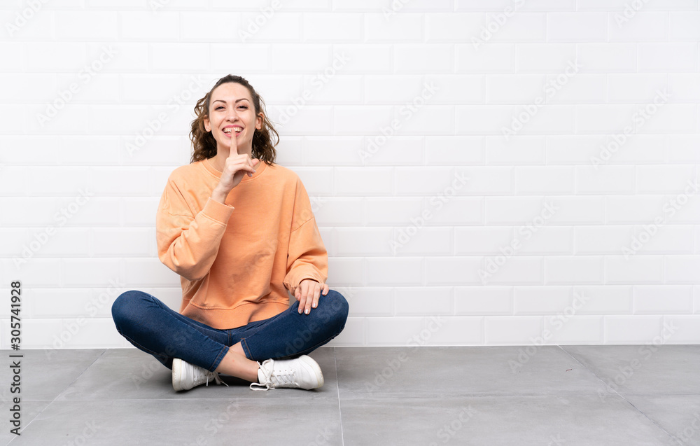 Young woman with curly hair sitting on the floor doing silence gesture Young woman with curly hair sitting on the floor doing silence gesture