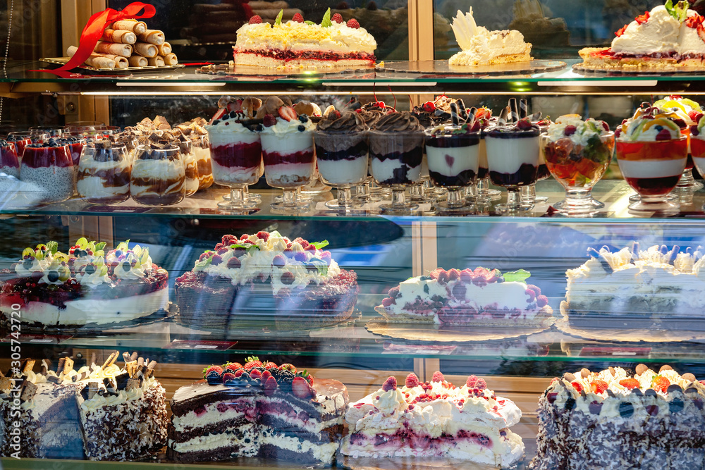 A variety of desserts and cakes in the window of a pastry shop in Krakow. Reflection of the buildings opposite in the shop window
