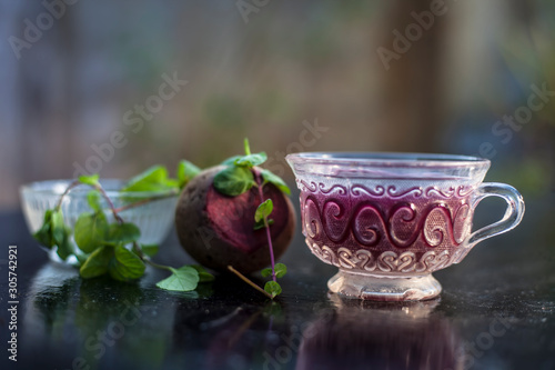 Best detoxify drink on a black glossy surface in a glass cup. Beetroot tea in a transparent glass cup on a black surface with a raw beet and some mint leaves. Horizontal shot with blurred background. photo