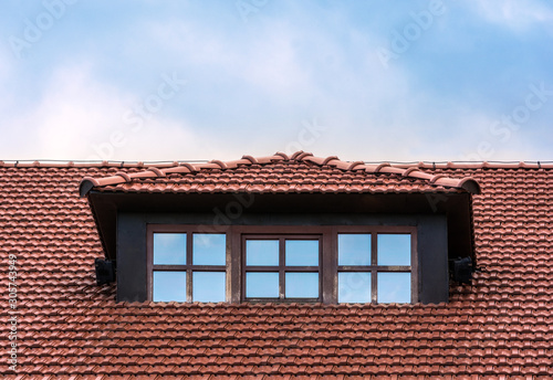The roof of the house is tiled. Window on the roof of the house. Attic. Blue cloudy sky.
