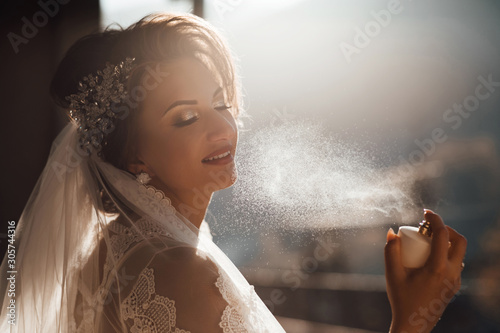 Bride applying perfume. Bride applying perfume on her neck. Sexy bride. Wedding day. Pretty young girl. Bride with luxurious hair and makeup.