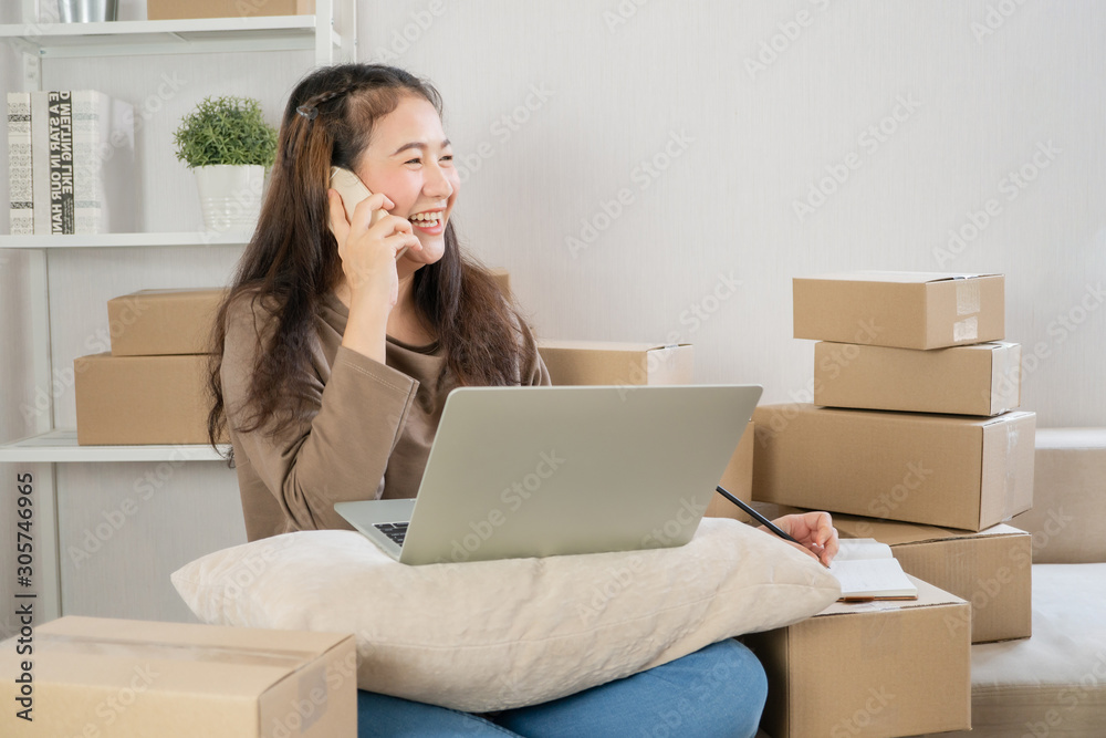 Happy Asian young entrepreneur, talking on the smartphone with customer for tack order, She smile for sales success at home office, Concept of merchant business online and eCommerce Happy Asian young entrepreneur, talking on the smartphone with customer for tack order, She smile for sales success at home office, Concept of merchant business online and eCommerce