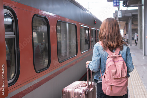Young traveller girl in jeans jacket with pink bag and luggage waiting for the train on the platform, copy space, travel or transportation concept