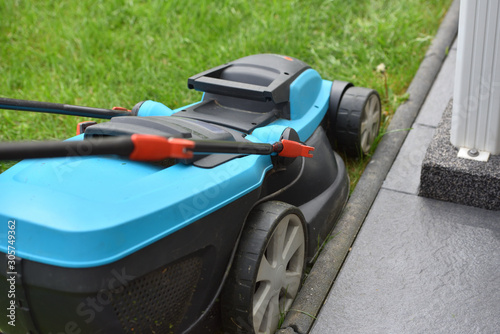 An electric lawn mower cuts the lawn near the edge and concrete curb. Close-up