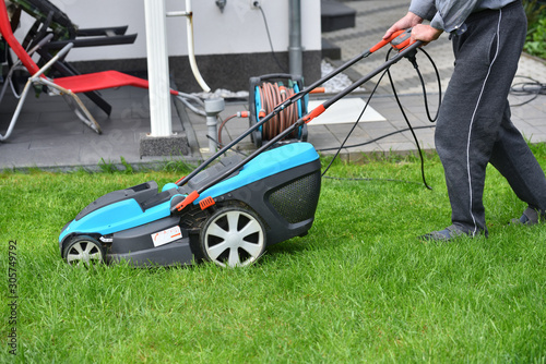 A man mows the lawn in his garden with an electric mower, close-up