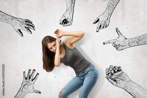 Young girl bending down covering her face with her hands trying to protect herself from mens' fists, finger guns and hands pointing at her. photo