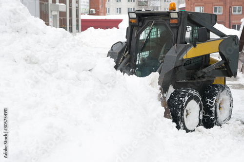 Snow drift. Snow plow compact tractor rakes a large snowdrift. Copy space.