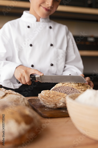Crop baker cutting fresh bread