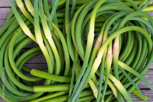 Green stalks of garlic on wooden table. The twisted stems of plants from seed. Preparation of summer salad for healthy diet