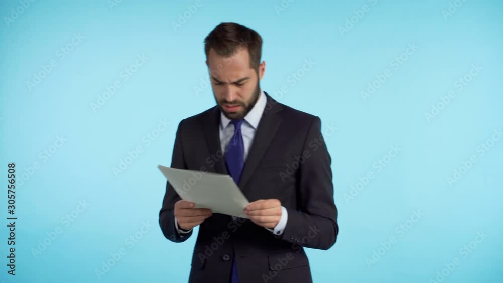 Serious businessman boss isolated on blue background studio. Man is unsatisfied with work of staff. Young mature male office employee in suit jacket checking documents, reports Serious businessman boss isolated on blue background studio. Man is unsatisfied with work of staff. Young mature male office employee in suit jacket checking documents, reports