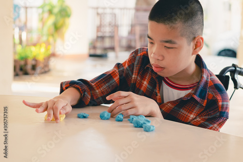 Asian disabled child on wheelchair molding clay, Fun and entertaining activity for training small and large muscles, Lifestyle in the education age of special need kids, Happy disability kid concept. photo