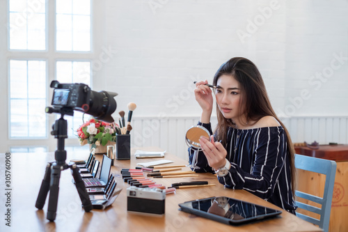 Asian woman blogger with makeup cosmetics recording video clip by smartphone at home.