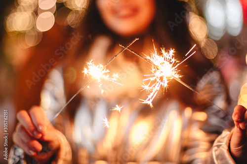 Young woman holding sparklers while standing against Christmas lights in city