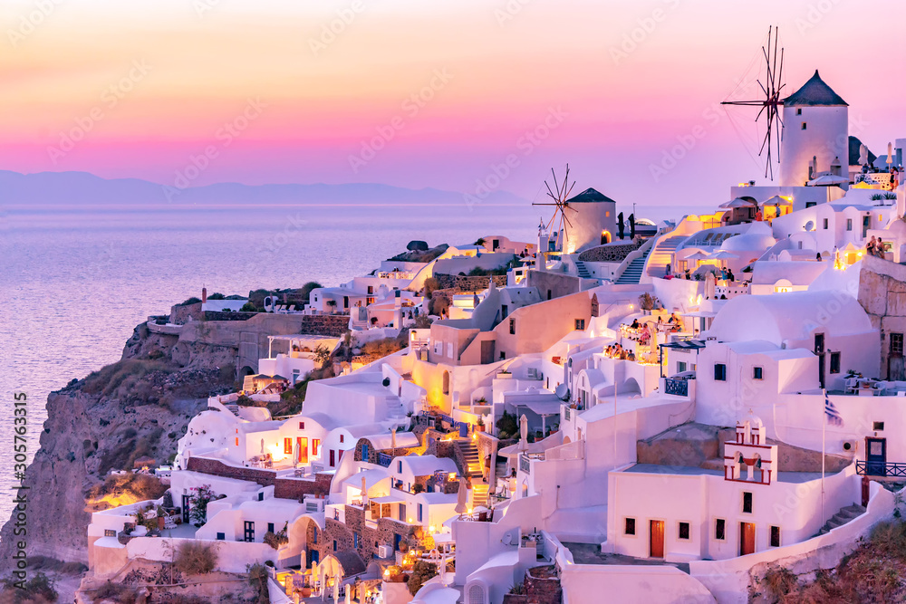 Fototapeta premium Beautiful view of Oia village with traditional white architecture and windmills in Santorini island in Aegean sea at sunset, Greece. Scenic travel background.