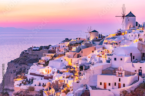 Beautiful view of Oia village with traditional white architecture and windmills in Santorini island in Aegean sea at sunset, Greece. Scenic travel background.
