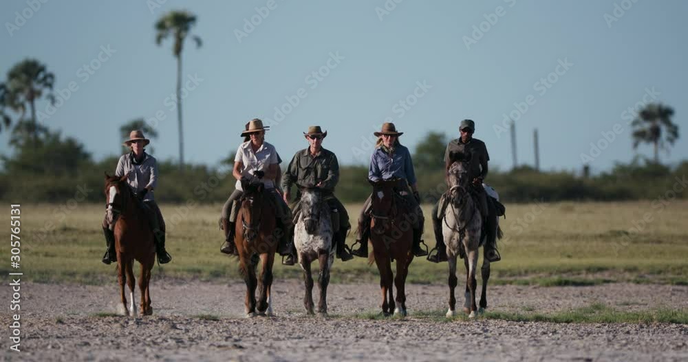 A Group of horse riders having fun galloping towards the camera across the wide open spaces of the Makgadikgadi salt Pans with blue skies in the background