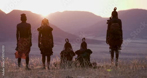 4K view of people from the Himba tribe in traditional dress, watching the sun setting on the mountains, Namib desert, Namibia photo