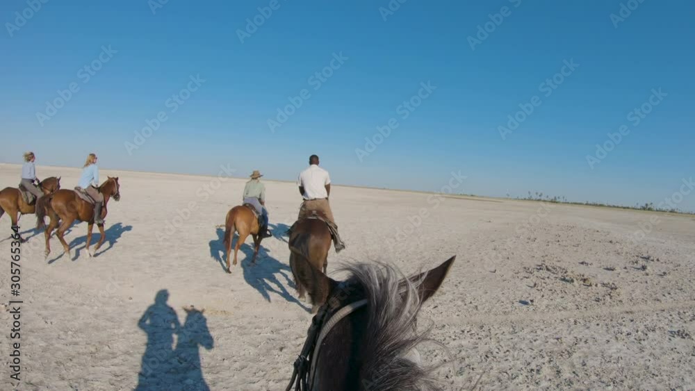 Slow motion view of a group of horse riders on safari cantering across the wide open spaces of the Makgadikgadi salt Pans  
