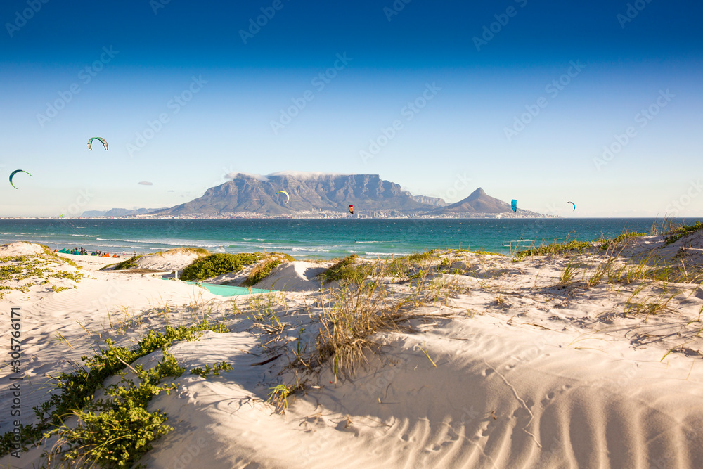 Fototapeta premium Beach dunes and kite surfers at Blouberg beach with in the background Cape Town and Table Mountain
