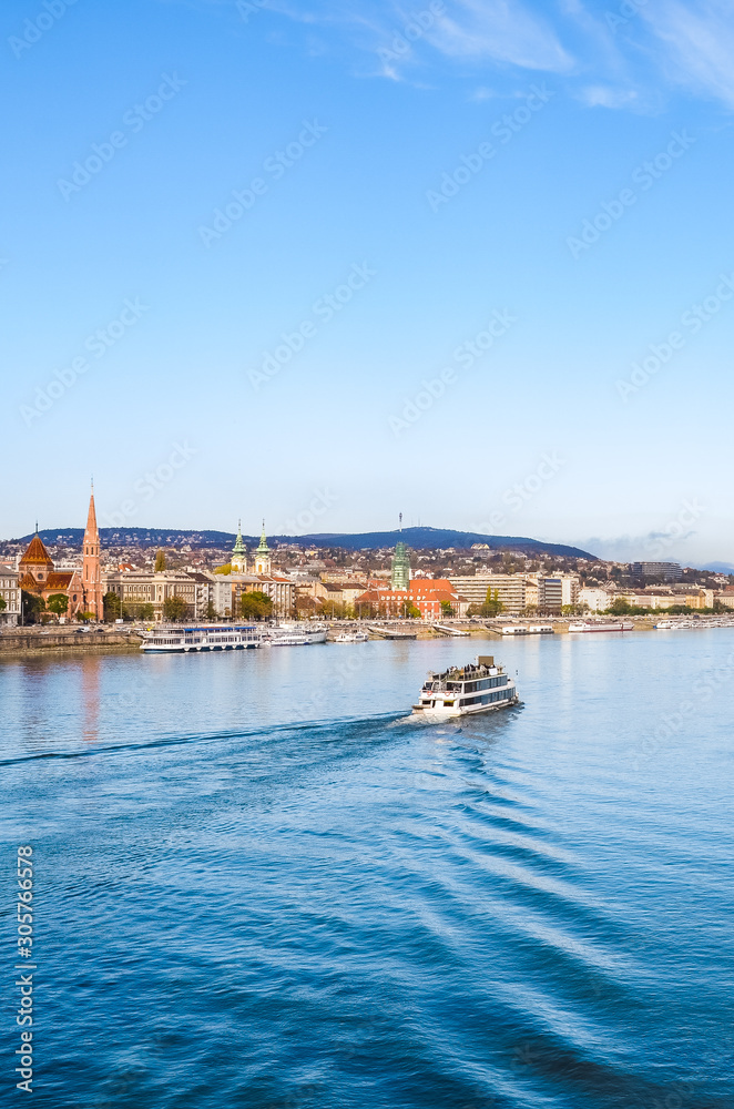 Vertical photo of the Danube river in Budapest, Hungary. Boat on the water. Historical buildings on along the river. Hungarian capital city cityscape. Eastern Europe