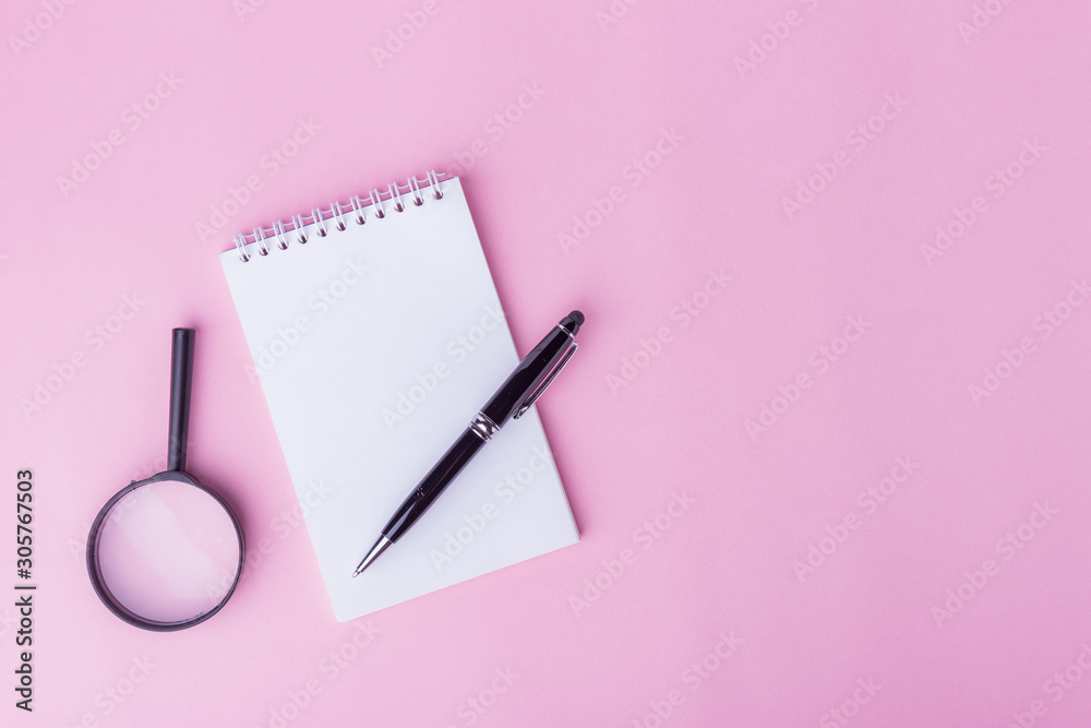 Flaylat workspace concept. An open notepad, pen and magnifying glass on pink background with copy space. Sweet soft colored tone. Flaylat workspace concept. An open notepad, pen and magnifying glass on pink background with copy space. Sweet soft colored tone.