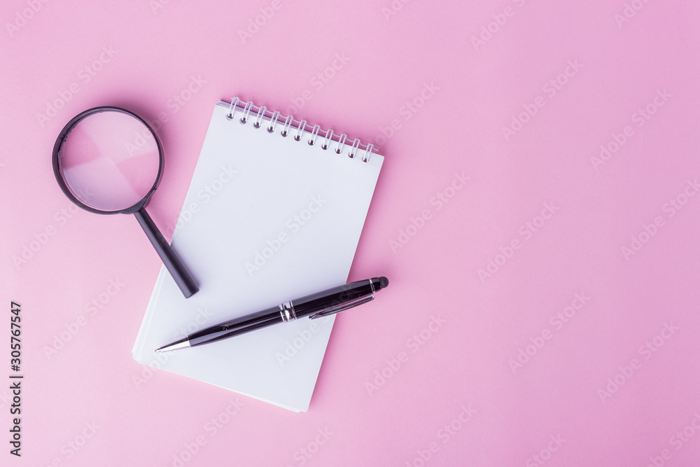 Flaylat workspace concept. An open notepad, pen and magnifying glass on pink background with copy space. Sweet soft colored tone. Flaylat workspace concept. An open notepad, pen and magnifying glass on pink background with copy space. Sweet soft colored tone.