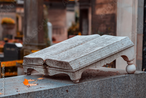 Old stone open book monument in the most famous cemetery of Paris Pere Lachaise, France. Tombs of various famous people. Golden autumn over eldest tombs.