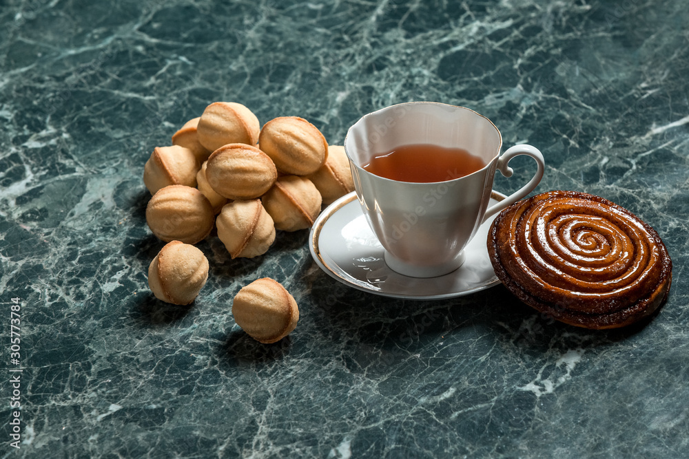 cinnamon bun with saucer, black tea and cookie walnut on marble background cinnamon bun with saucer, black tea and cookie walnut on marble background