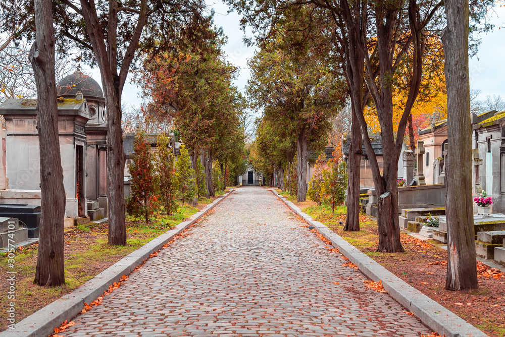 A view on autumn alley of the most famous cemetery of Paris Pere Lachaise, France. Tombs of various famous people. Golden autumn over eldest tombs.