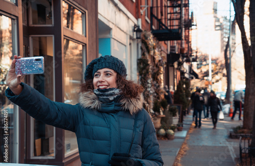 Beautiful curly brunette woman taking selfie self-portrait in Bleecker street, Greenwich Village, while sightseeing new york during winter season. Teal and orange color graded. photo