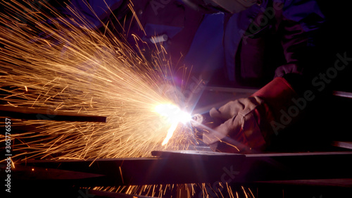 Worker in gloves cutting sheet metal in fabrication factory. Gas metal cutting with acetylene or oxygen torch. Bright sparks and smoke from exothermic reaction between oxygen and the workpiece in indu