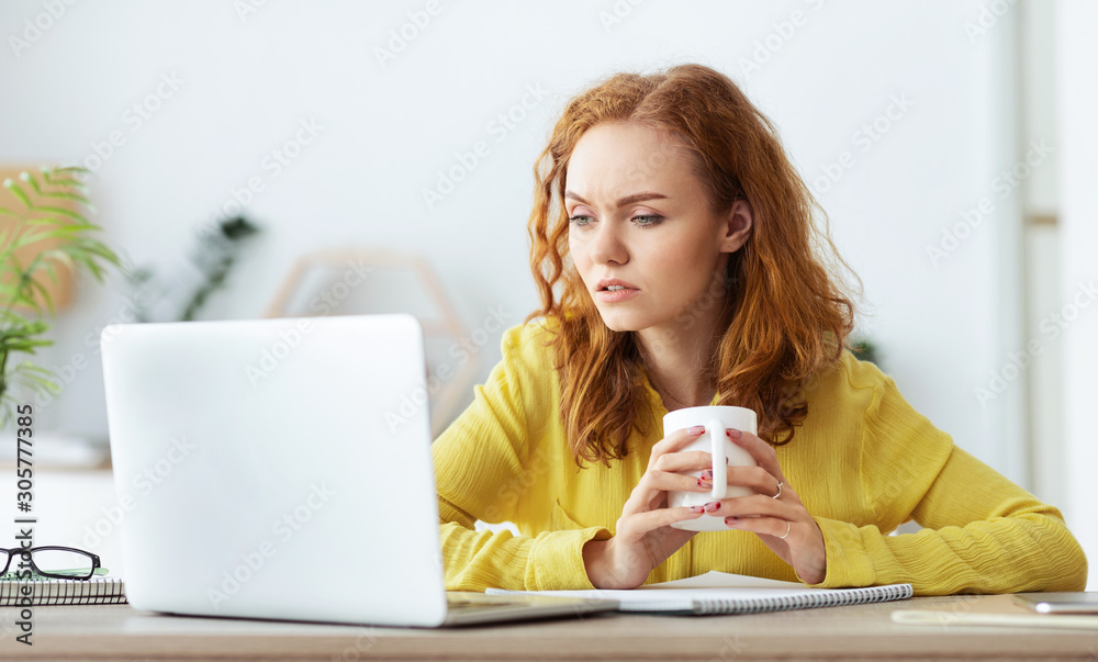 Serious girl reading news on laptop and drinking coffee Serious girl reading news on laptop and drinking coffee