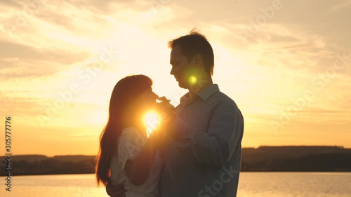 Young couple dancing at sunset on beach. Loving man and woman dance in bright rays of sun on background of the lake. Happy guy and girl waltz in the evening in the summer park.