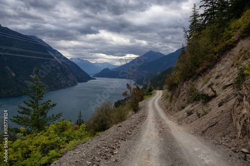 Beautiful view of a Dirt Road in the Mountain Valley near a lake during a cloudy summer evening. Taken on Anderson Lake Rd, near Lillooet, BC, Canada.