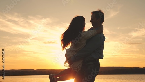 Happy guy and girl waltz in evening in the summer park. Loving man and woman dance in bright rays of sun on the background of the lake. Young couple dancing at sunset on beach.