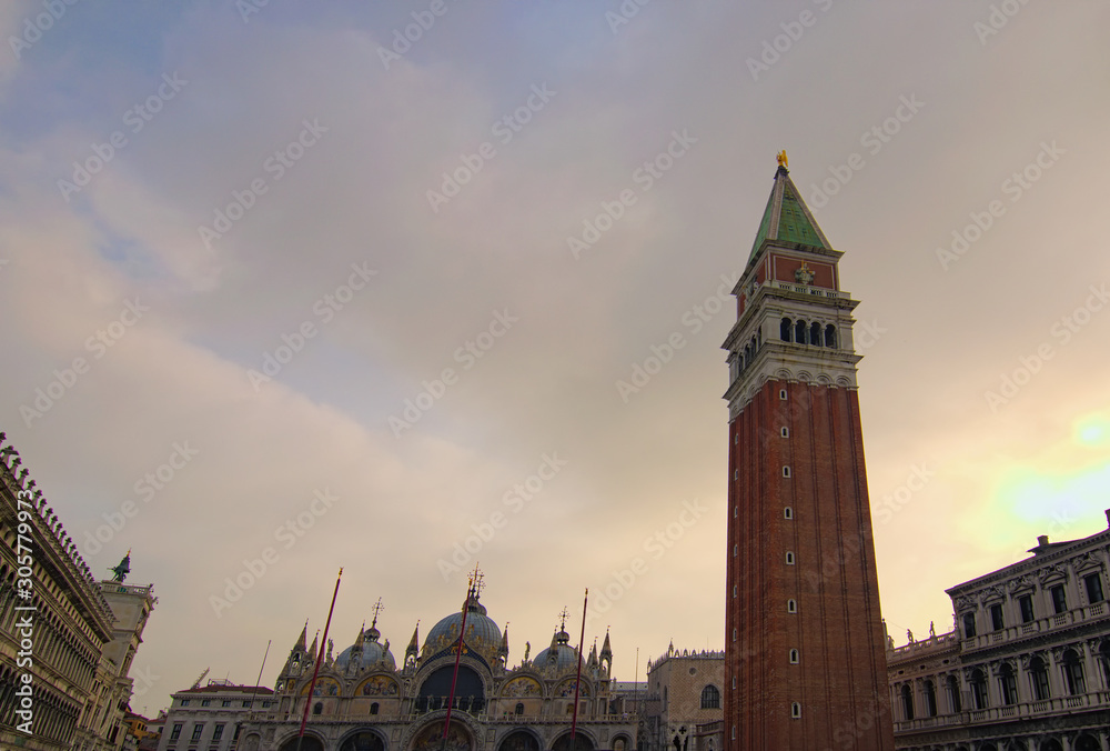 Picturesque landscape view of the high section of The Patriarchal Cathedral Basilica of Saint Mark with red brick tower and other medieval buildings against blue sky. Piazza San Marco, Venice, Italy