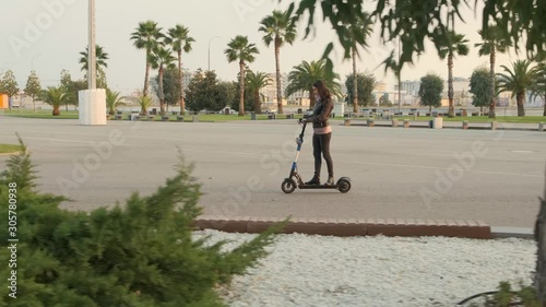 Riding in the Park on the electric scooter. The woman in the brunette rides his electric skateboard on the road. Following the shot.