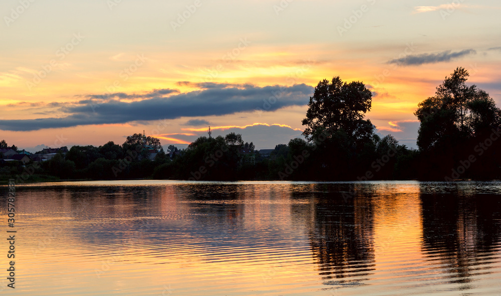 bright summer sunset on a lake with backlit clouds yellow red twilight