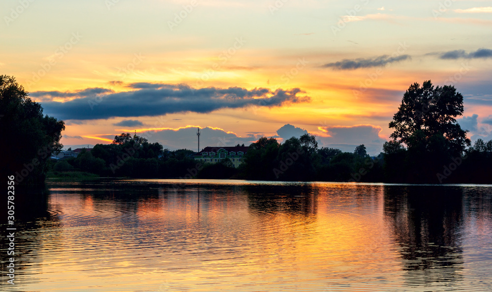 bright summer sunset on a lake with backlit clouds yellow red twilight