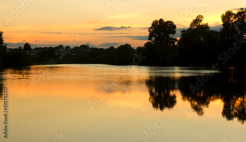 bright summer sunset on a lake with backlit clouds yellow red twilight © Irina
