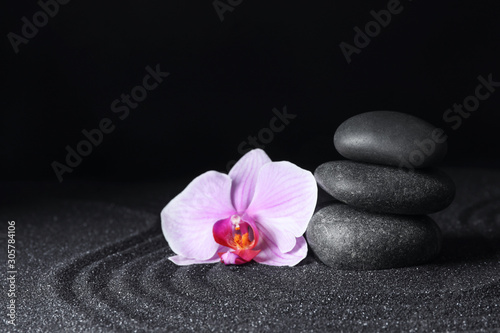 Spa stones and orchid flower on black sand with beautiful pattern, space for text. Zen concept