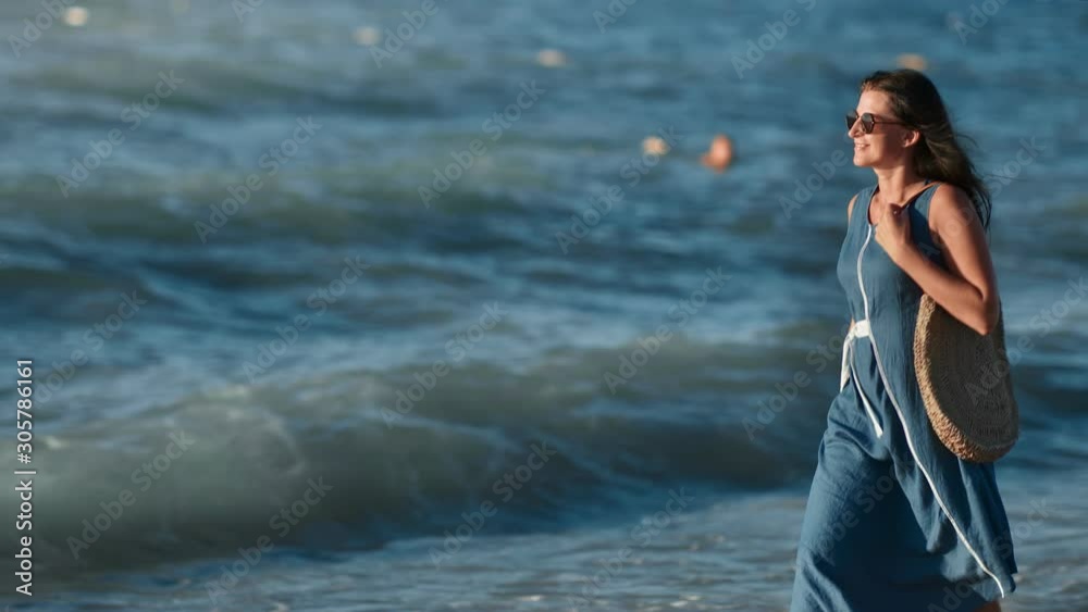 Attractive stylish tourist female walking on beach in sea wave background at sunset Attractive stylish tourist female walking on beach in sea wave background at sunset